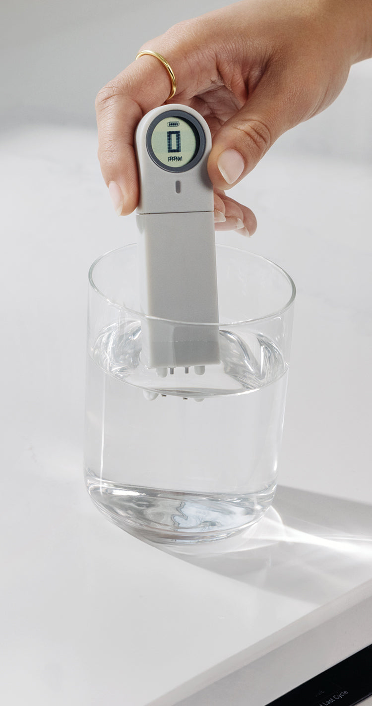 woman wearing ring testing water in glass with total dissolved solids meter