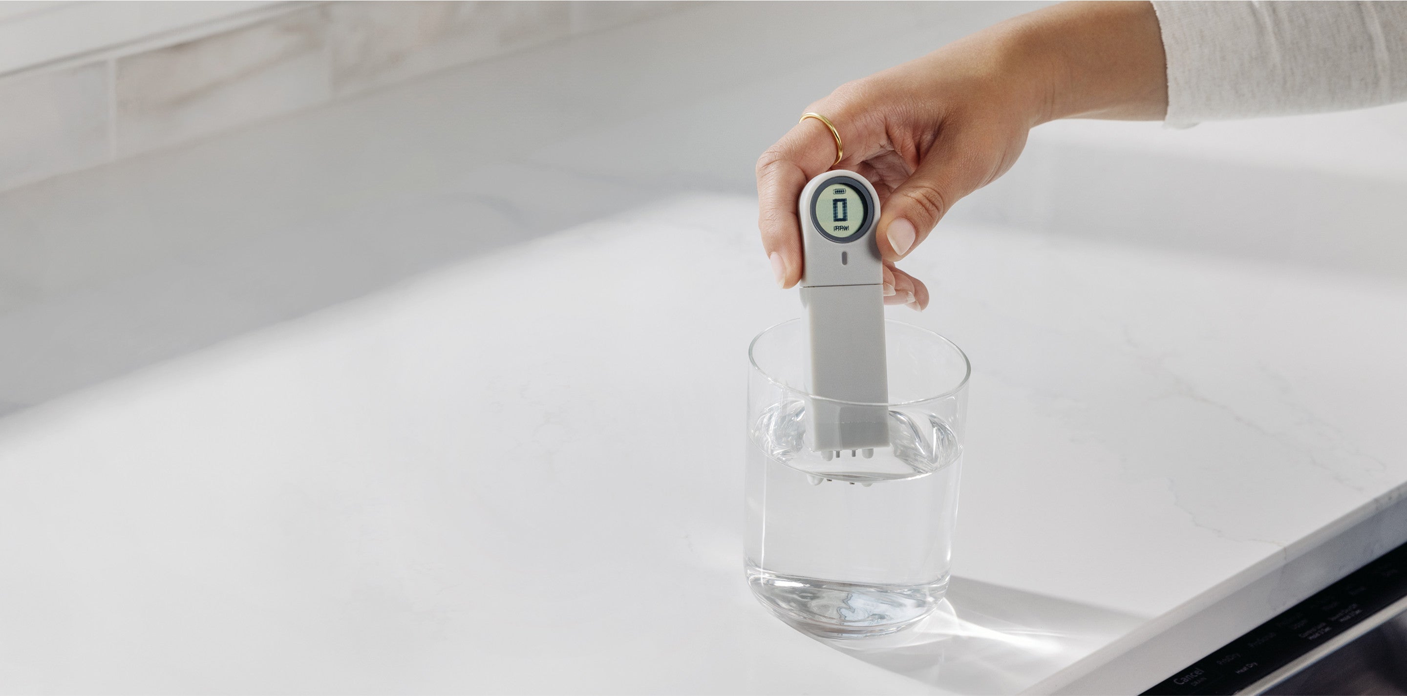 woman testing glass of water on counter with TDS meter