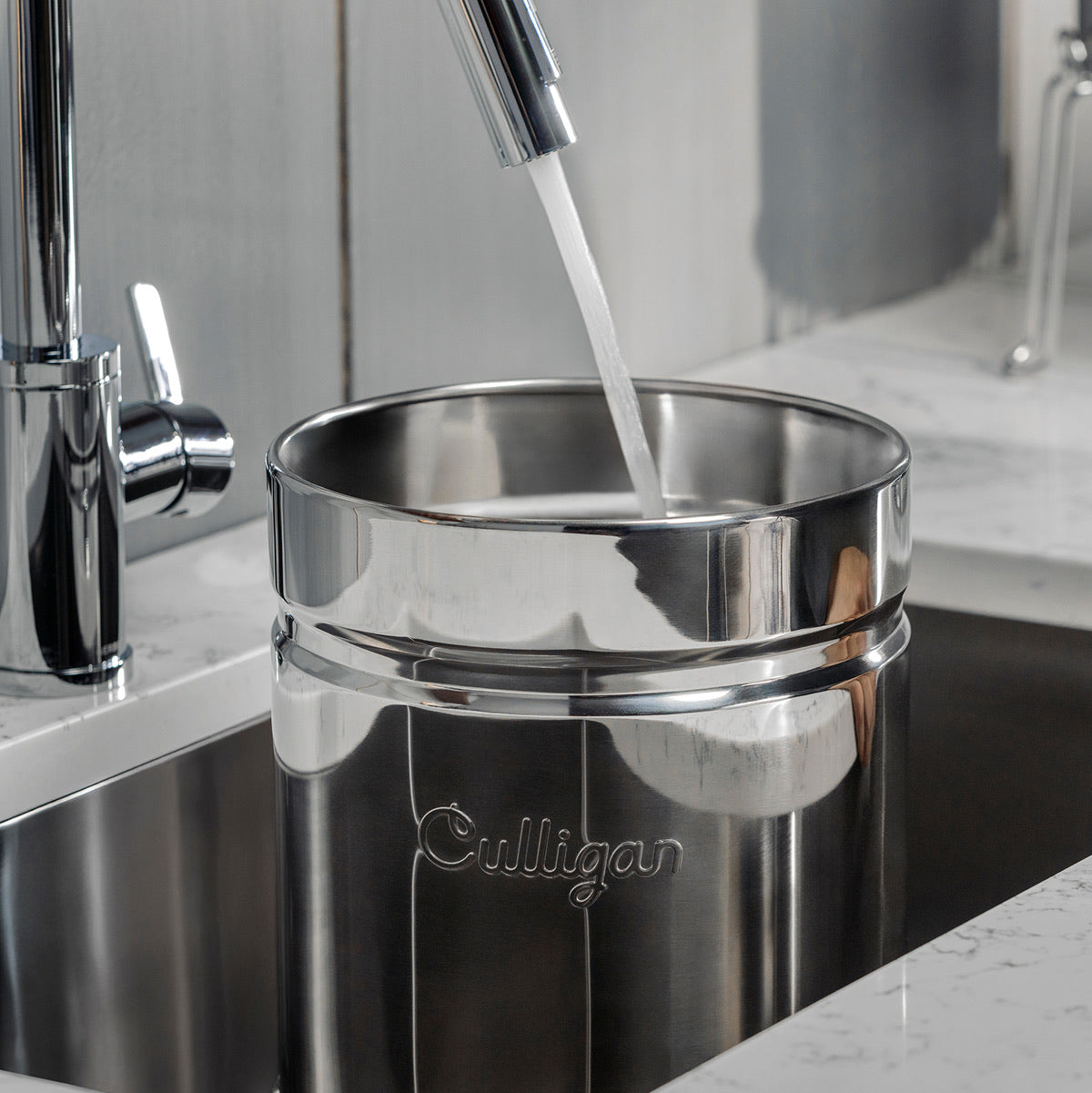 Culligan gravity water filter being filled with water from a faucet in a kitchen setting.