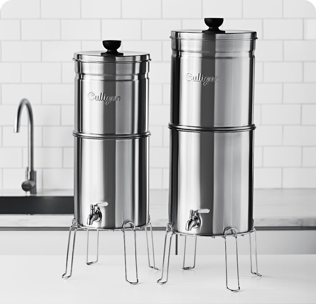 Two Culligan gravity water filters on a kitchen counter with a tiled wall background.